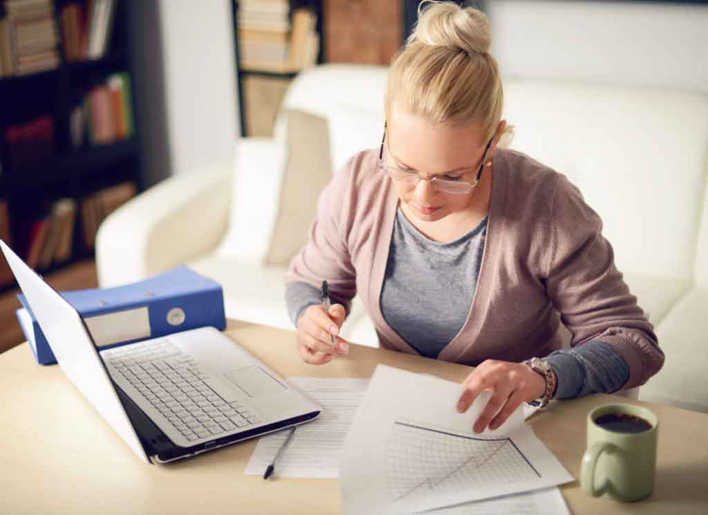 A blonde lady working on papers next to a laptop