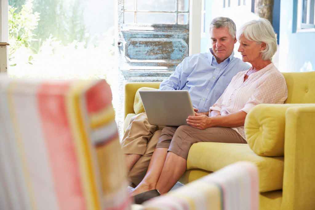 Senior Couple At Home In Lounge Using Laptop Computer